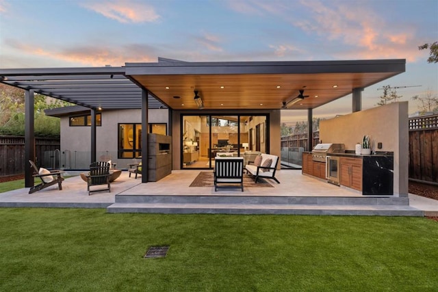 back house at dusk featuring exterior kitchen, a yard, an outdoor living space, and ceiling fan