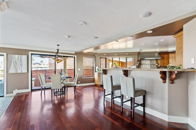 kitchen with light stone countertops, wall chimney range hood, dark hardwood / wood-style floors, kitchen peninsula, and a breakfast bar