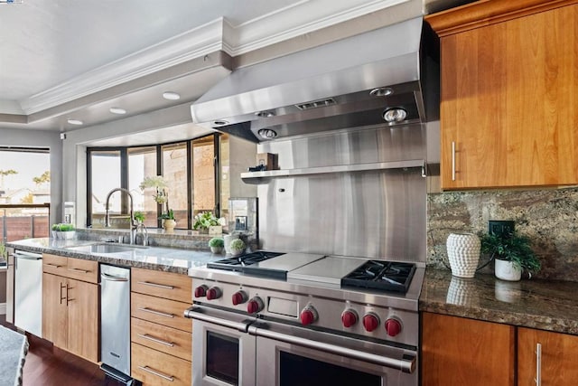 kitchen with sink, wall chimney exhaust hood, dark stone countertops, range with two ovens, and ornamental molding