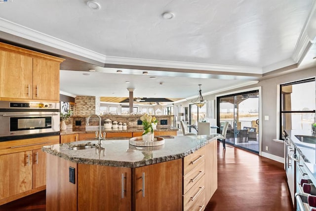 kitchen featuring stainless steel oven, sink, dark hardwood / wood-style flooring, crown molding, and an island with sink