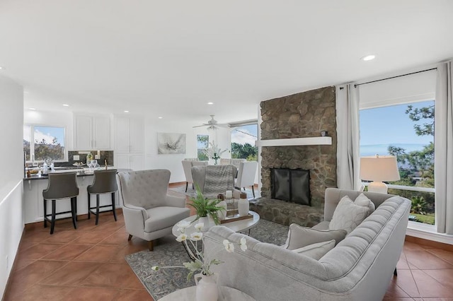 tiled living room featuring ceiling fan, a healthy amount of sunlight, and a stone fireplace