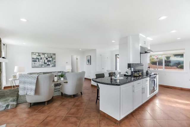 kitchen featuring white cabinetry, dark stone countertops, a breakfast bar, and dark tile patterned floors