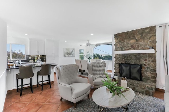 living room featuring ceiling fan, tile patterned floors, and a stone fireplace