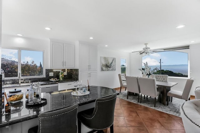 kitchen with ceiling fan, decorative backsplash, white cabinetry, dark tile patterned floors, and dark stone counters