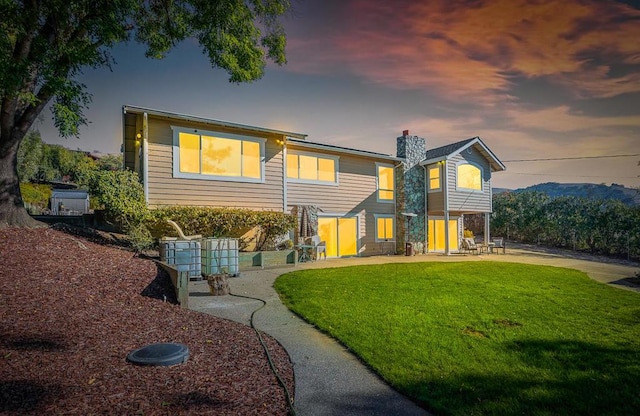 back house at dusk featuring a lawn