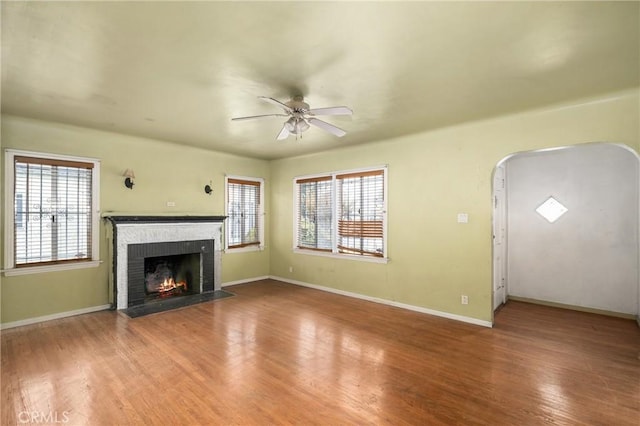 unfurnished living room with a fireplace, wood-type flooring, ceiling fan, and a healthy amount of sunlight