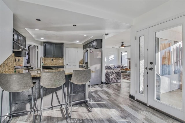 kitchen with tasteful backsplash, kitchen peninsula, wood-type flooring, sink, and stainless steel fridge