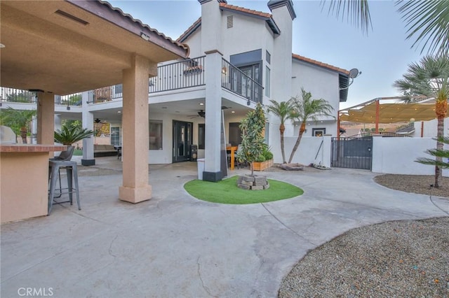 back of house with ceiling fan, a patio area, a balcony, and an outdoor bar