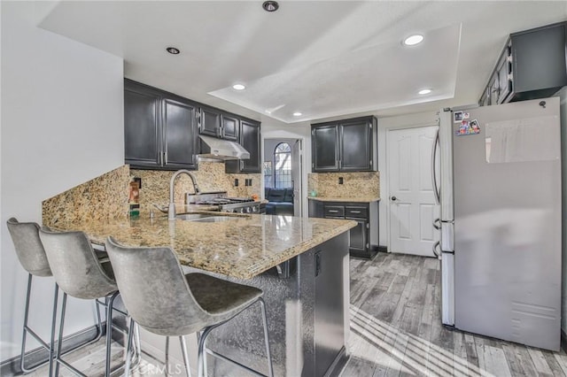 kitchen with kitchen peninsula, a kitchen bar, stainless steel refrigerator, light wood-type flooring, and light stone counters