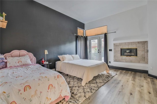 bedroom featuring access to outside, a tile fireplace, and light hardwood / wood-style floors