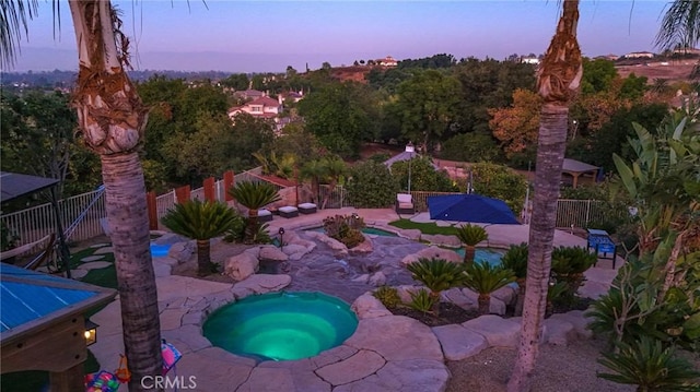 pool at dusk with an in ground hot tub and a patio