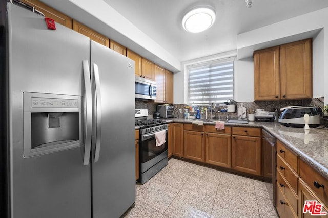 kitchen with sink, dark stone countertops, backsplash, and appliances with stainless steel finishes