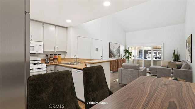 kitchen featuring white appliances, sink, vaulted ceiling, light wood-type flooring, and kitchen peninsula