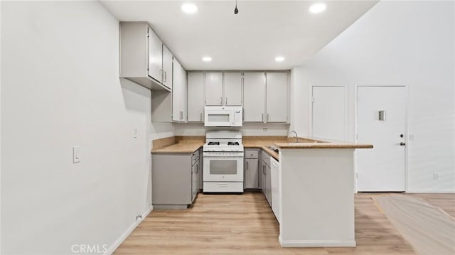 kitchen with sink, light wood-type flooring, white appliances, and kitchen peninsula