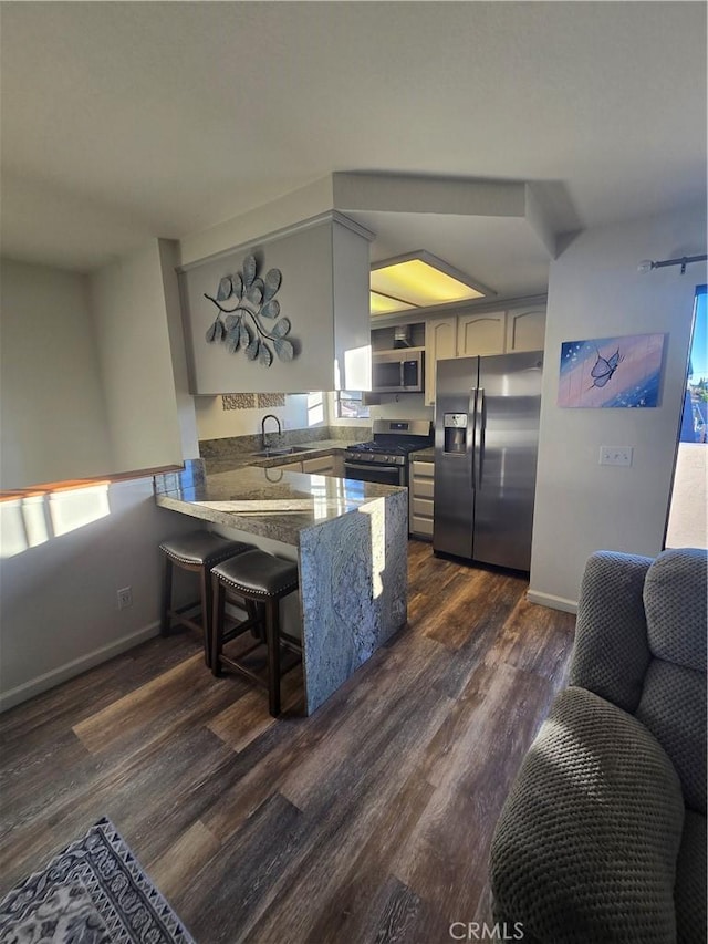 kitchen featuring kitchen peninsula, appliances with stainless steel finishes, a kitchen breakfast bar, dark hardwood / wood-style flooring, and sink