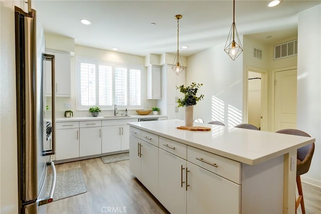 kitchen featuring white cabinets, stainless steel fridge, a center island, and sink