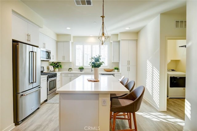 kitchen featuring a breakfast bar, stainless steel appliances, a center island, washer / clothes dryer, and white cabinetry