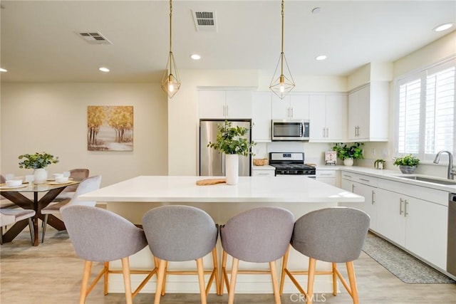 kitchen with sink, hanging light fixtures, a kitchen island, white cabinetry, and stainless steel appliances