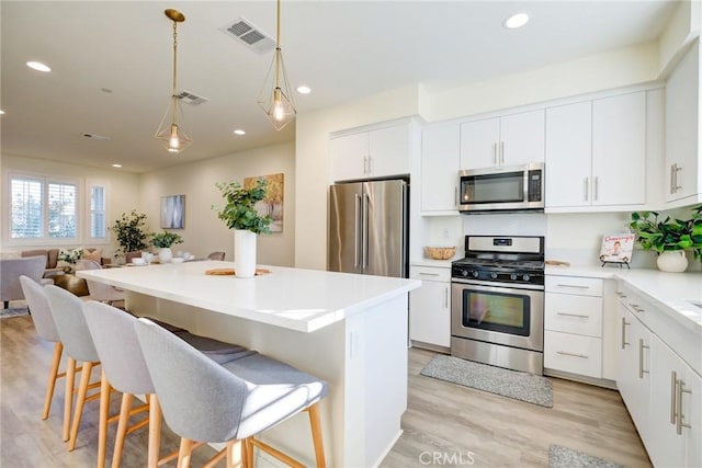 kitchen with a kitchen bar, white cabinetry, light wood-type flooring, and appliances with stainless steel finishes