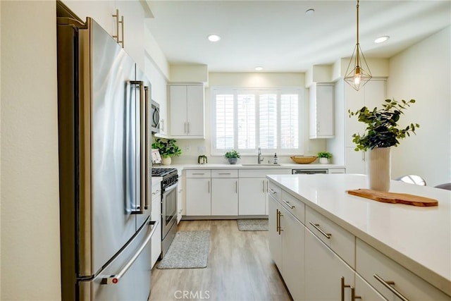 kitchen with appliances with stainless steel finishes, light hardwood / wood-style floors, white cabinetry, and hanging light fixtures