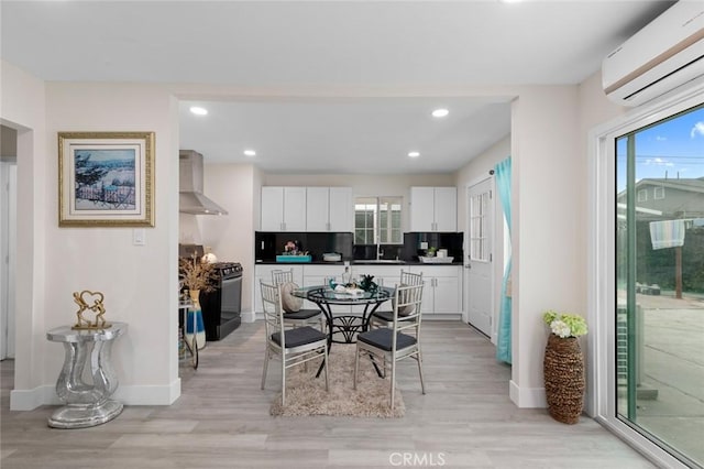 kitchen with white cabinets, gas range, light wood-style flooring, a wall mounted air conditioner, and wall chimney range hood