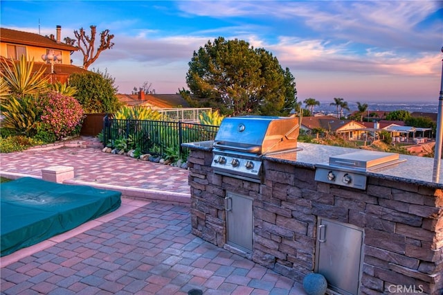 patio terrace at dusk featuring area for grilling and an outdoor kitchen