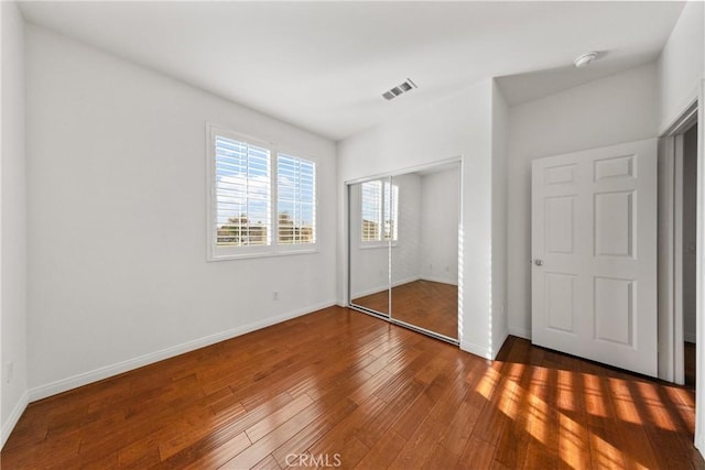 unfurnished bedroom featuring a closet, visible vents, baseboards, and hardwood / wood-style floors