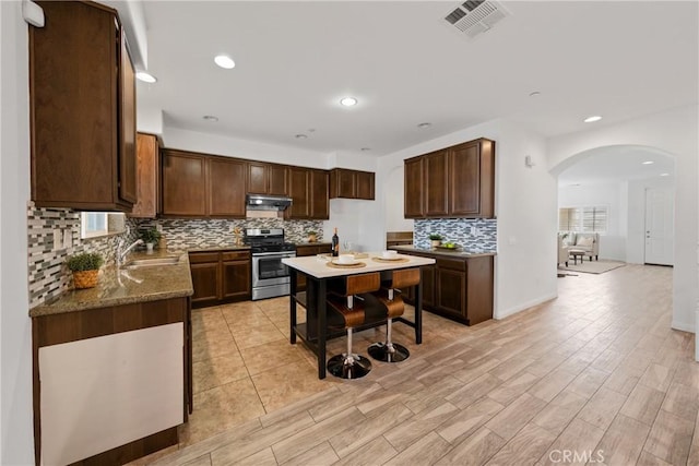 kitchen with arched walkways, stainless steel gas range oven, under cabinet range hood, a sink, and visible vents