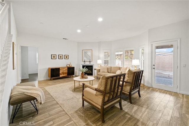 living room featuring light wood finished floors, visible vents, baseboards, a glass covered fireplace, and recessed lighting