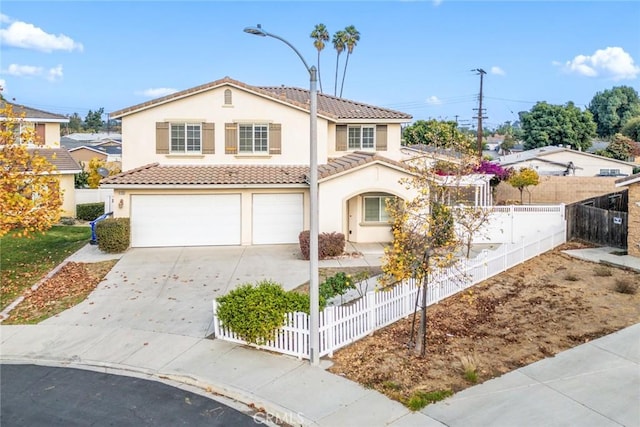 mediterranean / spanish-style home featuring a fenced front yard, an attached garage, a tile roof, driveway, and stucco siding