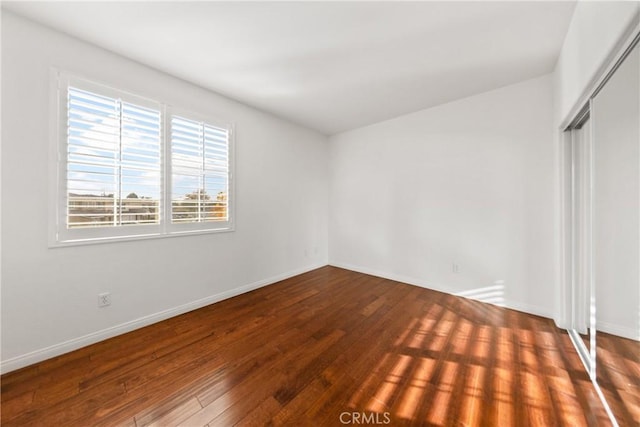 unfurnished bedroom featuring a closet, wood-type flooring, and baseboards