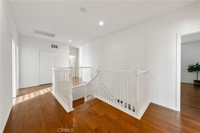 hallway with visible vents, wood-type flooring, and an upstairs landing