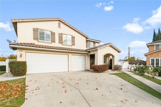 mediterranean / spanish home with a garage, fence, concrete driveway, a tiled roof, and stucco siding