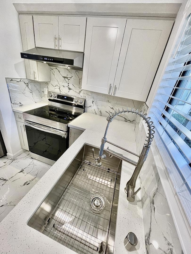 kitchen featuring stainless steel electric stove, white cabinetry, tasteful backsplash, and light stone countertops