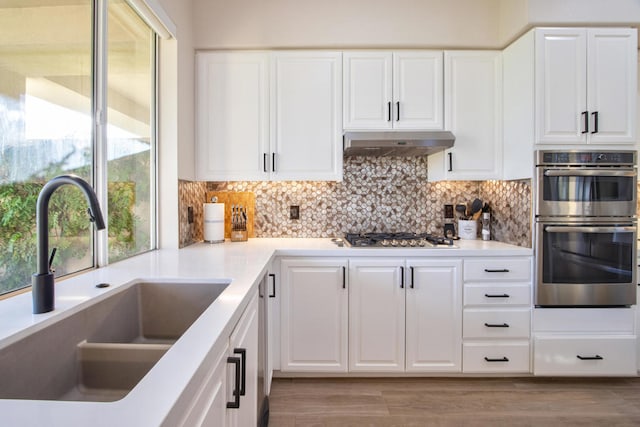 kitchen featuring backsplash, white cabinets, sink, appliances with stainless steel finishes, and light hardwood / wood-style floors