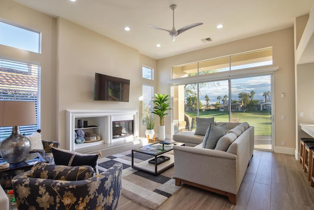 living room featuring ceiling fan, plenty of natural light, a towering ceiling, and light hardwood / wood-style flooring