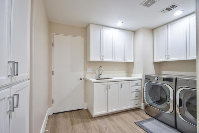 clothes washing area featuring cabinets, separate washer and dryer, light hardwood / wood-style floors, and sink