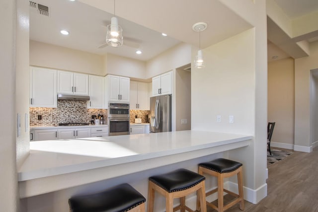 kitchen featuring kitchen peninsula, hardwood / wood-style flooring, appliances with stainless steel finishes, decorative light fixtures, and white cabinetry