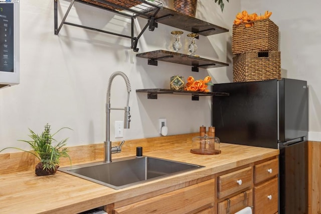 kitchen with wooden counters, black refrigerator, and sink