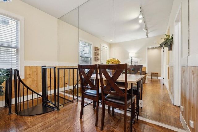 dining area with rail lighting, hardwood / wood-style flooring, and wood walls