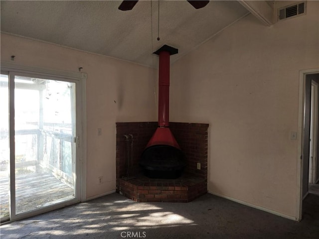 unfurnished living room with carpet, a wood stove, vaulted ceiling with beams, ceiling fan, and a textured ceiling