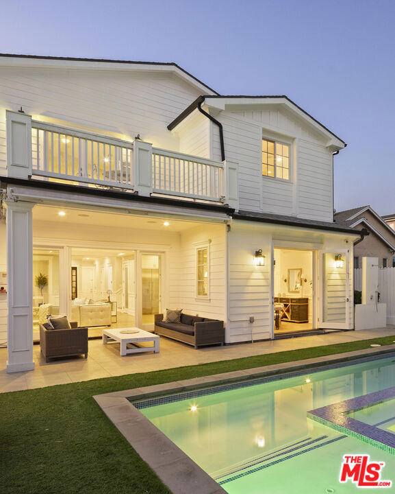 back house at dusk with outdoor lounge area, a pool with hot tub, and a balcony