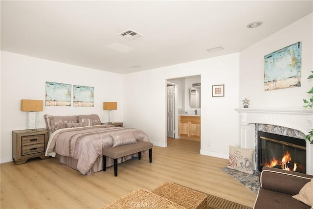 bedroom with light wood-type flooring, a fireplace, and connected bathroom