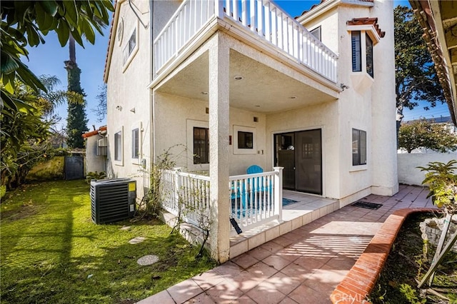 back of property with a lawn, cooling unit, a balcony, and a patio area