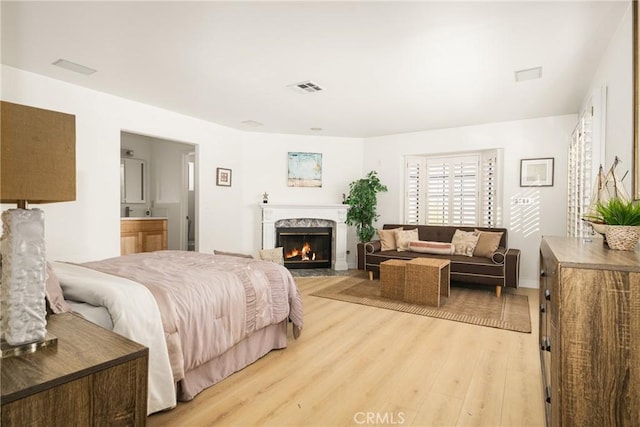 bedroom with ensuite bathroom, light wood-type flooring, and a high end fireplace