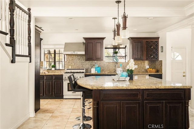 kitchen featuring a center island, dark brown cabinetry, wall chimney range hood, and stainless steel stove