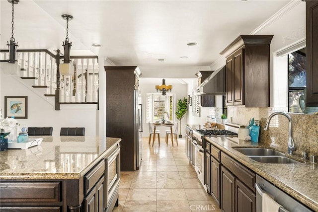 kitchen with sink, hanging light fixtures, wall chimney range hood, an inviting chandelier, and appliances with stainless steel finishes