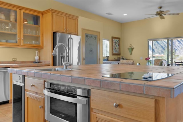 kitchen featuring sink, ceiling fan, light tile patterned floors, tile counters, and stainless steel appliances