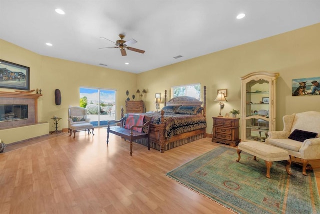 bedroom with a tiled fireplace, ceiling fan, and light hardwood / wood-style floors