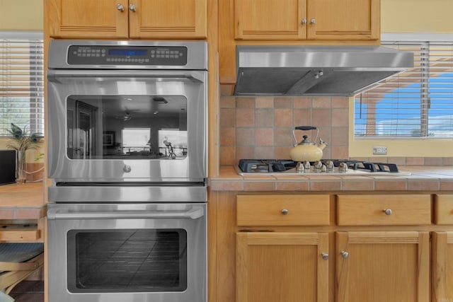 kitchen with tile countertops, decorative backsplash, extractor fan, and appliances with stainless steel finishes